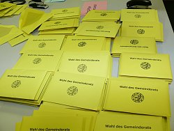 Auf einem Tisch liegen viele gelbe Umschläge mit der Aufschrift &#34;Wahl des Gemeinderats&#34; und darunter das Wappen der Stadt Lahr.