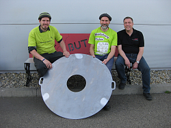 Geschäftsführer Achim Redt der Firma BUT (rechts) übergibt die Grillplatte an Andreas Hummel (links) und Michael Kempf (mitte) vom Spielplatzteam.
Sie sitzen auf einer Bank, das Spielplatzteam trägt grüne T-Shirts, Herr Redt ein schwarzes Poloshirt. 