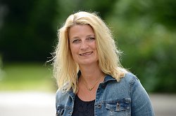 Portraifoto von Ulrike Karl. Sie hat blonde lange Haare und trägt eine Jeansjacke und eine goldene Halskette. Im Hintergrund Grün.