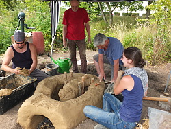 Studenten stehen um einen aus Lehm geformente Töpferofen. 