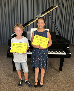 Die zwei Schüler der Städtischen Musikschule Lahr stehen vor einem Flügel und halten stolz ihre geleben Urkunden in die Kamera. 