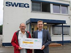 Der Gewinner und Wolfgang Bumann stehen vor dem SWEG - Gebäude mit einer überdimensionalen Fahrkarte in den Händen und lächeln. 