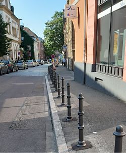 Das Bild zeigt einen Blick in die Schillerstraße. Entlang des Gehwegs rechts sind neue dunkelgraue Poller einbetoniert. links parken Autos.
