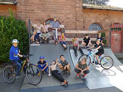 Zu sehen sind 15 Kinder auf und um eine Skateboardrampe im Schlachthof Lahr. Sie lachen und schneiden teilweise Grimassen. Zwei Kinder, die auf der Rampe sitzen, haben Sonnenblumen in der Hand.