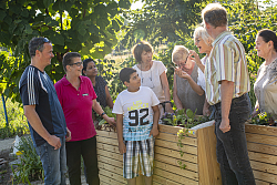 Auf dem Bild erläutert Frau Waltraud Stark einem Teil der Gärtnerinnen und Gärtnern des Interkulturellen Gartens und Frau Eva Schilling von der Firma Wagner System die Bepflanzung der drei gespendeten Hochbeete. 