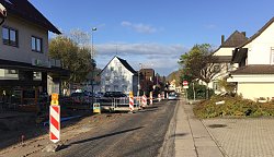 Das Bild zeigt einen Blick auf die Baustelle Ortsdurchfahrt Reichenbach. Die Asphaltdecke der Straße ist abgetragen. Die STraße wird von rot-weißen Warnbaken und Absperrbändern gesäumt. Zu den geschäften führen Baustellenbrücken.