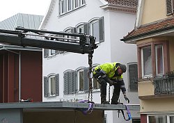 Ein Mitarbeiter des BGL mit gelber Arbietsjacke steht auf dem Dach eines Chrysanthema Häuschens, um ein demontiertes Teil an einen Kran anzuhängen.