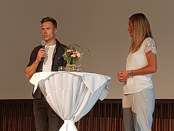 Markus Rehm hält das Mikro in der Hand, daneben Moderatorin Senja Töpfer. 