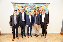 Das Foto zeigt fünf Männer vor einem bunten Bild. 