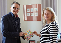 Markus Ibert steht links mit einem blauen Anzug und lächelt in die Kamera. Er hält eine selbstgebastelte Laterne in der Hand, die er Ulrike Karl zeigt. Sie steht links im gestreiften Pulli. 