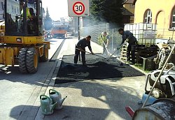 Mitarbeiter der Firma Trenkle bei Asphaltarbeiten an einer Bushaltestell bei der Friedrichschule in Lahr. Links im Bild ist ein gelber Bagger.