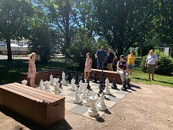 Das Foto zeigt zwei Mädchen, die im Freien auf einer großen Fläche Schach spielen. Vier weiter Personen beobachten die Mädchen dabei.