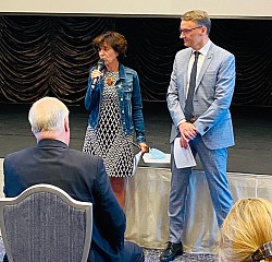 OB Markus Ibert und die Bürgermeisterin von Gerstheim Laurence Muller-Bronn stehen bei der deutsch-französischen Verkehrskonferenz gemeinsam vor den Teilnehmenden. Frau Muller-Bronn hält ein Mikrofon in der Hand.
