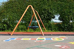 Korbschaukel auf dem Pausenhof Hort Luisenschule, dahinter grüne Büsche, im Vordergrund auf dem Asphalt eine bunte Kinderzeichnung