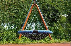 Korbschaukel auf dem Pausenhof Hort Luisenschule, im Hintergrund grüne Büsche