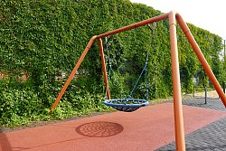 Eine Korbschaukel auf dem Pausenhof Hort Luisenschule hängt an einem orangen Metallgestell, im Hintergrund grüne Büsche