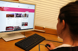 Vor einem Bildschirm, das das Schülertraining von Brockhaus zeigt, sitzt eine junge Frau und hält die Maus in in der Hand. Der Bildschirm zeigt typische englische Motive wie eine rote Telefonzelle oder ein Londoner Doppeldeckerbus. 