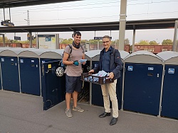Florian Fischer, in Fahrradfahrmontour und Oberbürgermeister markus Ibert stehen am Lahrer Bahnhof vor den Fahrradschließfächern. Herr Ibert hat einen Korb voller belegter Brötchen.