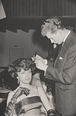 schwarz-weiß-Bild einer Frisurenschau in der Stadthalle aus dem Jahr 1962. eine Dame mit voluminöser Föhnwelle wird von einem Herrn im Anzug frisiert. 