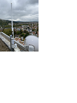 Das Foto zeigt eine Antenne auf einem Dach. Im Hintergrund ist eine Stadt zu sehen. 