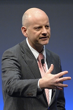 Portrait von Prof. Dr. Stephan Bierling, seitlich fotografiert. Er gestikuliert, trägt einen grau-weiß-gestreiften Anzug mit weißem Hemd mit rosa Krawatte. 