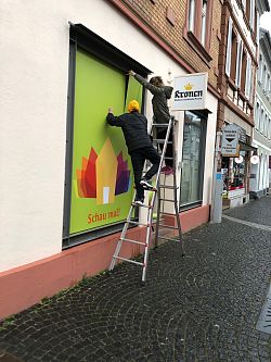Auf dem Bild sieht man Ralf Henning auf einer Leiter stehend beim Bekleben eines Schaufensters
