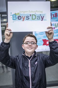 Das Foto zeigt einen Jungen, er hält ein Schild hoch über dem Kopf mit der Aufschrift BoysDay, Jungen Zukunftstag