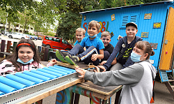 Kinder sitzen am Beginn der Rollenrutschen. Im Hintergrund ist das Spielmobil. 