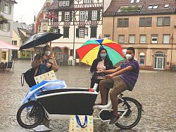 Klimaschutzmanagerin Madeleine Krol und Teilnehmer des Escape-Games auf dem Lahrer Marktplatz mit Regenschirmen und einem Lastenrad.