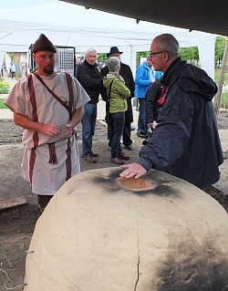 Prof. Heising steht neben dem römischen Töpferofen und hält seine Hand darüber. Daneben eine männliche Person, die in römischer Kleidung gewandet ist. 