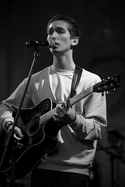 Das schwarz-weiß Foto zeigt Vincent Alexander bei einem Aufritt mit der Gitarre