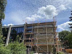 Außenfassede des Max-Planck-Gymnasiums mit einem Gerüst. Darüber blauer Himmel mit weißen Wolken.