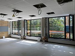 Fensterfront im Max-Planck-Gymnasium von innen fotografiert. Vor den Fenstern sieht man ein Baugerüst. Von der Decke hängen Kabel herab.