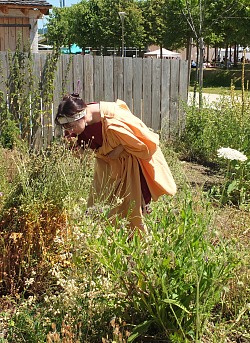 Eine junge Frau, in römischen Gewändern gekleidet, steht im archäobotanischen Garten und riecht an einer Pflanze. 