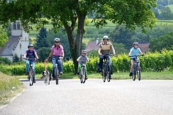 Zwei Erwachsene und drei Kinder auf dem Fahrrad, dazu ein angeleinter Hund.