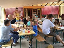 Kinder und Eltern sitzen auf Bierbänken und spielen Schach.