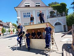 Die Gruppe Grundi der Jugendfeuerwehr der Stadt Lahr steht um und in einem hölzernen Verkaufsstand auf dem Rathausplatz. 