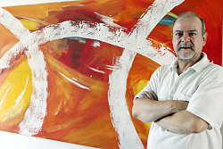 Armin Andreas Pangerl steht vor einem großformatigen Bild mit dicken weißen Linien vor gelb-orange-rotem Hintergrund.&#13;&#10;