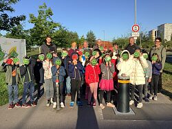 Kinder stehen am Eingang des Seeparks in Mietersheim, gemeinsam mit der Ortsvorsteherin und Ortschaftsräten.&#13;&#10;Sie halten ein grünes Lachsmiley vor das Gesicht. Einige wenige auch ein rotes Smiley mit heruntergezogenen Mundwinkeln.