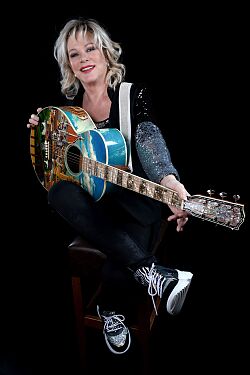 Lisa Fitz mit Gitarre, sie sitzt auf einem Barhocker