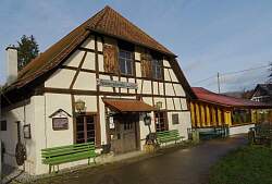 Fachwerkgebäude der Hammerschmiede in Reichenbach, davor zwei grüne Sitzbänke