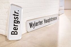 Zwei Straßenschilder lehnen an einer Wand. 