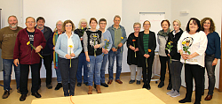 Teilnehmerinnen und Teilnehmer der Schulung stehen zum Gruppenbild und halten jeweils ein Blümchen in der Hand. 
