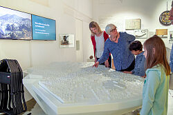 Zwei Frauen und zwei Kinder stehen vor einem weißen Stadtmodell.