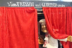 eine Puppe in Kochklamotten umschlungen von einem roten Vorhang 