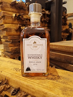 In einer großen eckigen Glasflasche ist ein gold-gelber Whiskey auf einem Holztresen in gelbem Licht zu sehen 