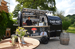 Unter freiem Himmel ist ein Foodtruck mit Blumen und einem Stehtisch im Vordergrund zu erkennen 