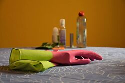 Im Vordergrund liegt ein Paar Gummihandschuhe in den Farben Grün und Pink. Im Hintergrund stehen Glasflaschen verschiedener Größe.