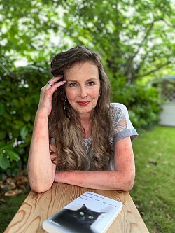 Sabeth Ackermann sitzt in einem Garten, auf dem Tisch vor ihr liegt ihr Roman.