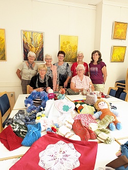 Gruppe von sieben Frauen steht hinter einem Tisch voller Handarbeiten.